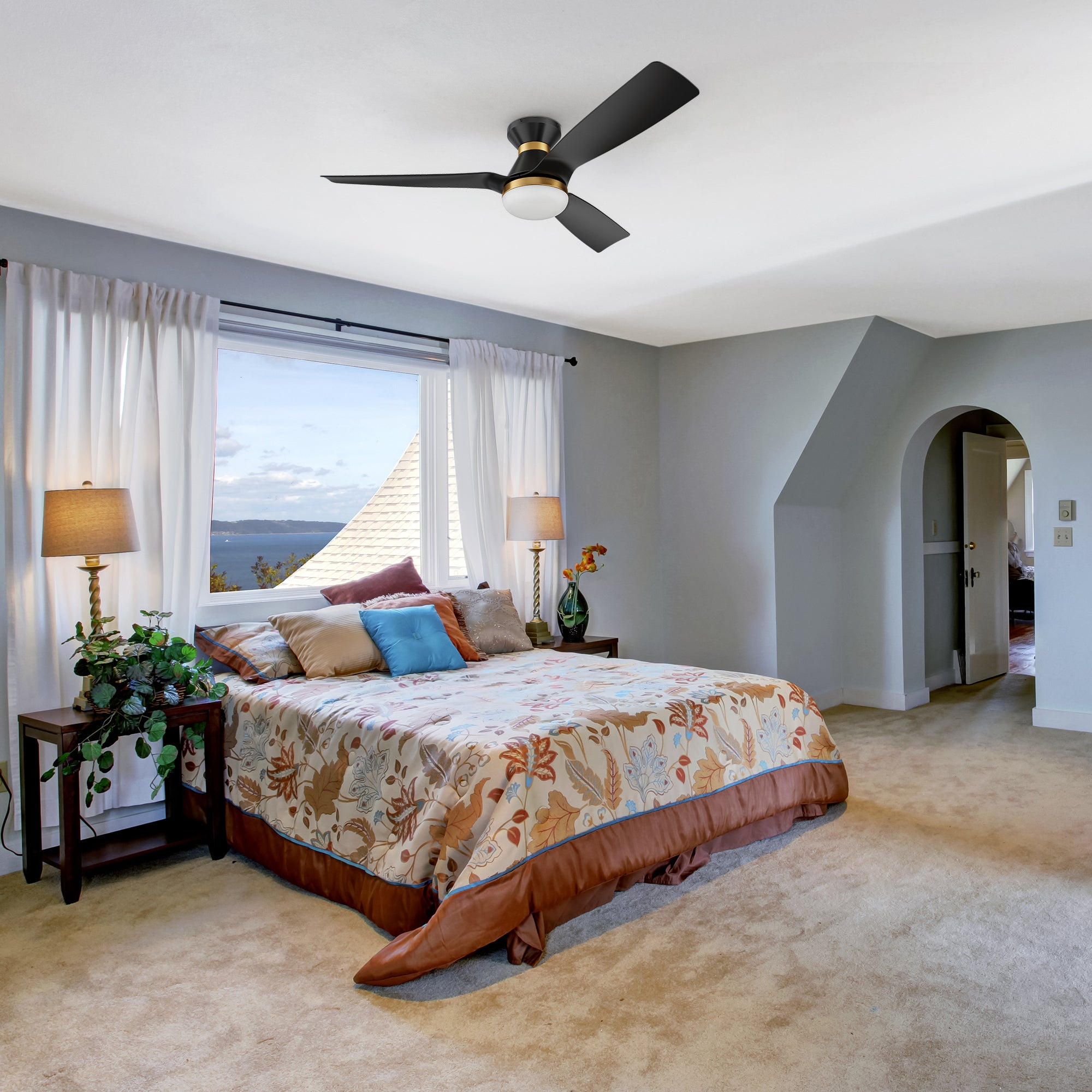 A modern bedroom featuring a Livex Black & Gold 52-inch Low Profile Smart Ceiling Fan with LED light and remote, mounted on a white ceiling for efficient airflow and cooling. The ceiling fan has black blades with gold accents, complementing the room&